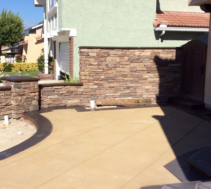 New custom entrance with colored concrete, stone covered pilasters, and concrete poured bull-nosed steps & wall cap that contrast with the light colored slab. Pacificland Constructors