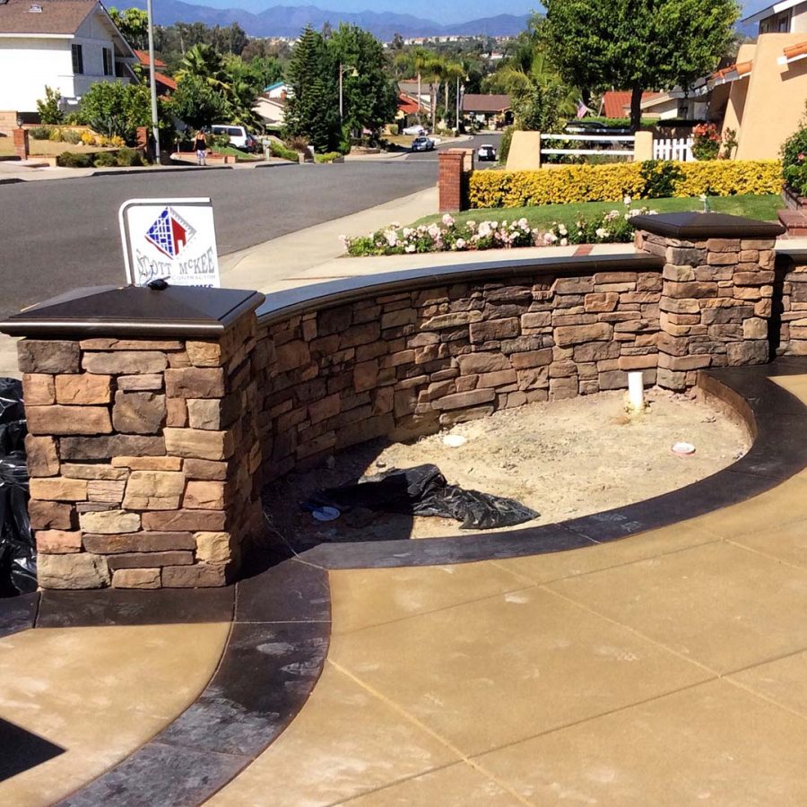 New custom entrance with colored concrete, stone covered pilasters, and concrete poured bull-nosed steps & wall cap that contrast with the light colored slab. Pacificland Constructors