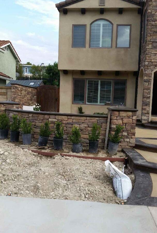 New custom entrance with colored concrete, stone covered pilasters, and concrete poured bull-nosed steps & wall cap that contrast with the light colored slab. Pacificland Constructors