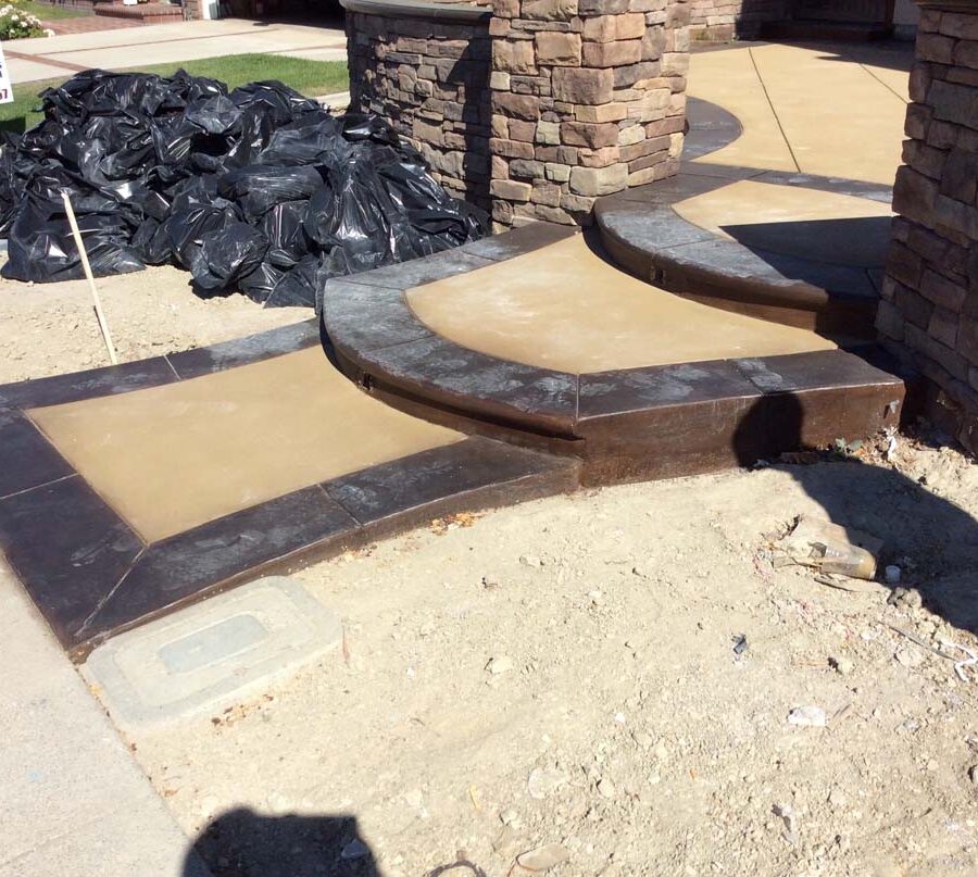 New custom entrance with colored concrete, stone covered pilasters, and concrete poured bull-nosed steps that contrast from the center of the slab. Pacificland Constructors