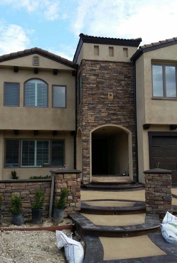 New custom entrance with colored concrete, stone covered pilasters, and concrete poured bull-nosed steps & wall cap that contrast with the light colored slab.