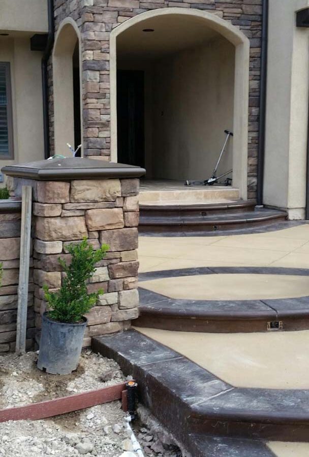 New custom entrance with colored concrete, stone covered pilasters, and concrete poured bull-nosed steps & wall cap that contrast with the light colored slab.