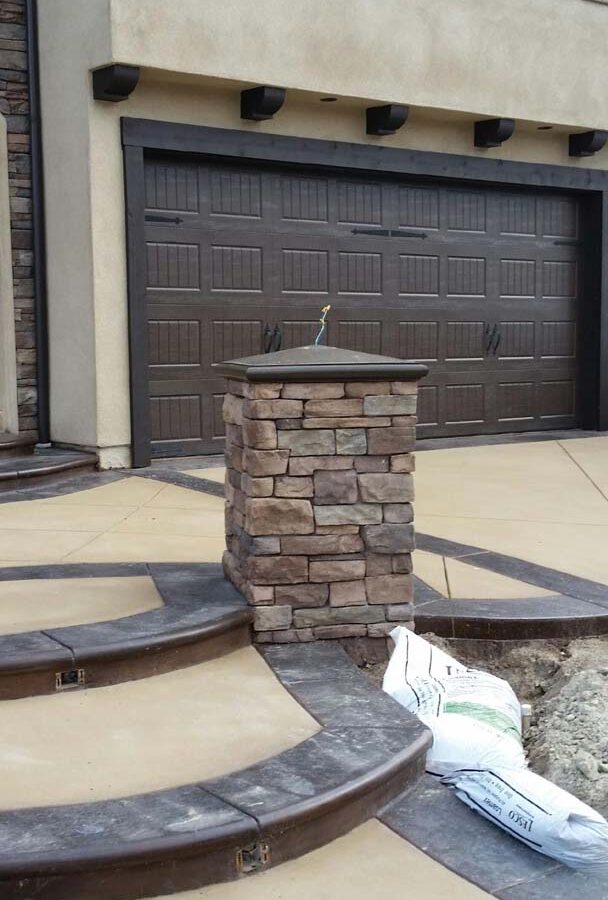 New custom entrance with colored concrete, stone covered pilasters, and concrete poured bull-nosed steps that contrast from the center of the slab.