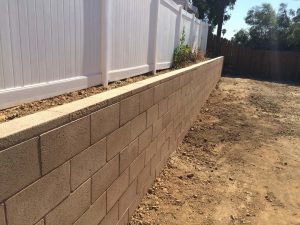 Small precision block retaining wall with wall cap creates more flat area for the home because it holds up the offset elevation between our clients and their neighbor’s side.