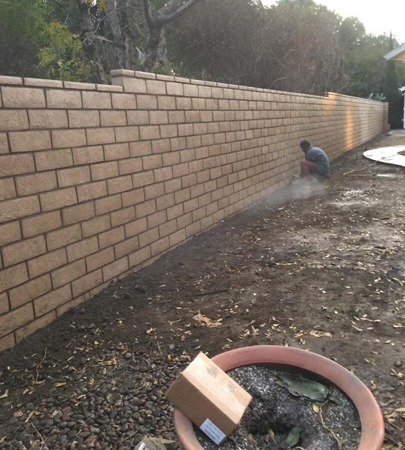 Construction of a new tan colored slump block freestanding wall for a backyard along the centerline of the property lines.