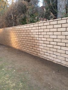 New tan colored slump block freestanding wall for a backyard along the centerline of the property lines.