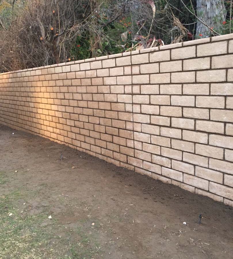 New tan colored slump block freestanding wall for a backyard along the centerline of the property lines.