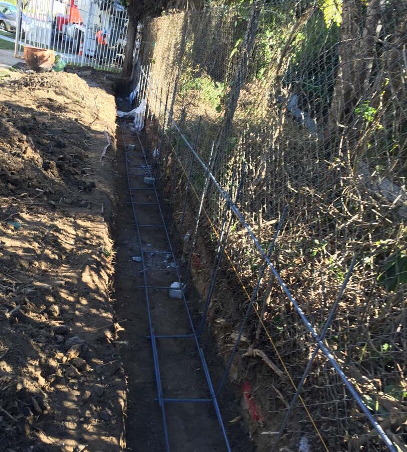 Construction of the strip footings. These are excavated, compacted, and reinforced with steel rebar prior to pouring concrete. This is fundamental for the structural integrity of the freestanding wall.