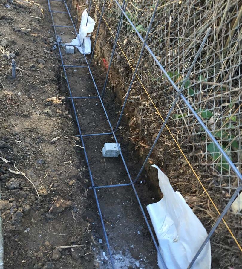 Construction of the strip footings. These are excavated, compacted, and reinforced with steel rebar prior to pouring concrete. This is fundamental for the structural integrity of the freestanding wall.