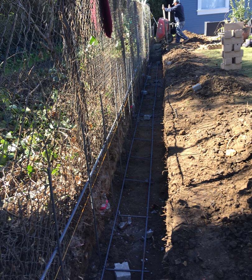 Construction of the strip footings. These are excavated, compacted, and reinforced with steel rebar prior to pouring concrete. This is fundamental for the structural integrity of the freestanding wall.