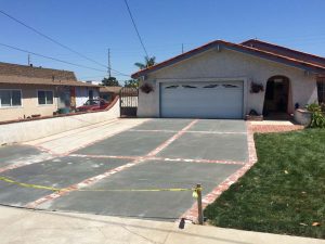 New broom swept gray concrete driveway with brick ribbons. Pacificland Constructors