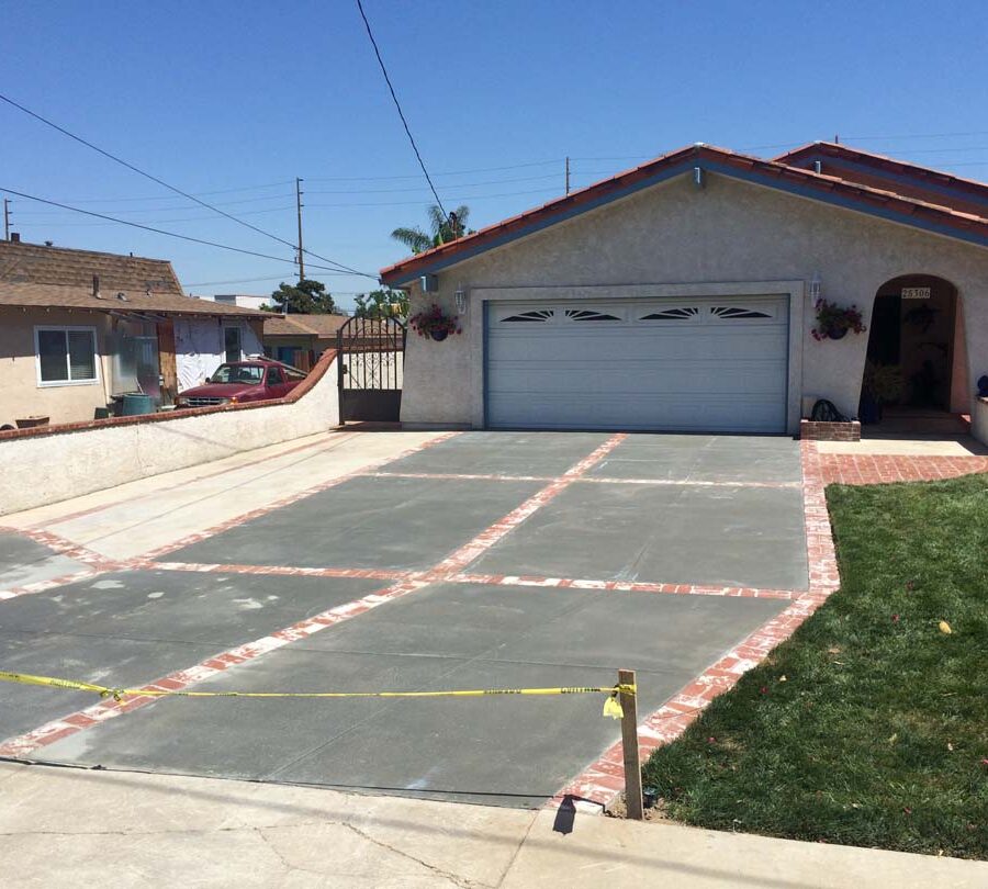 New broom swept gray concrete driveway with brick ribbons. Pacificland Constructors