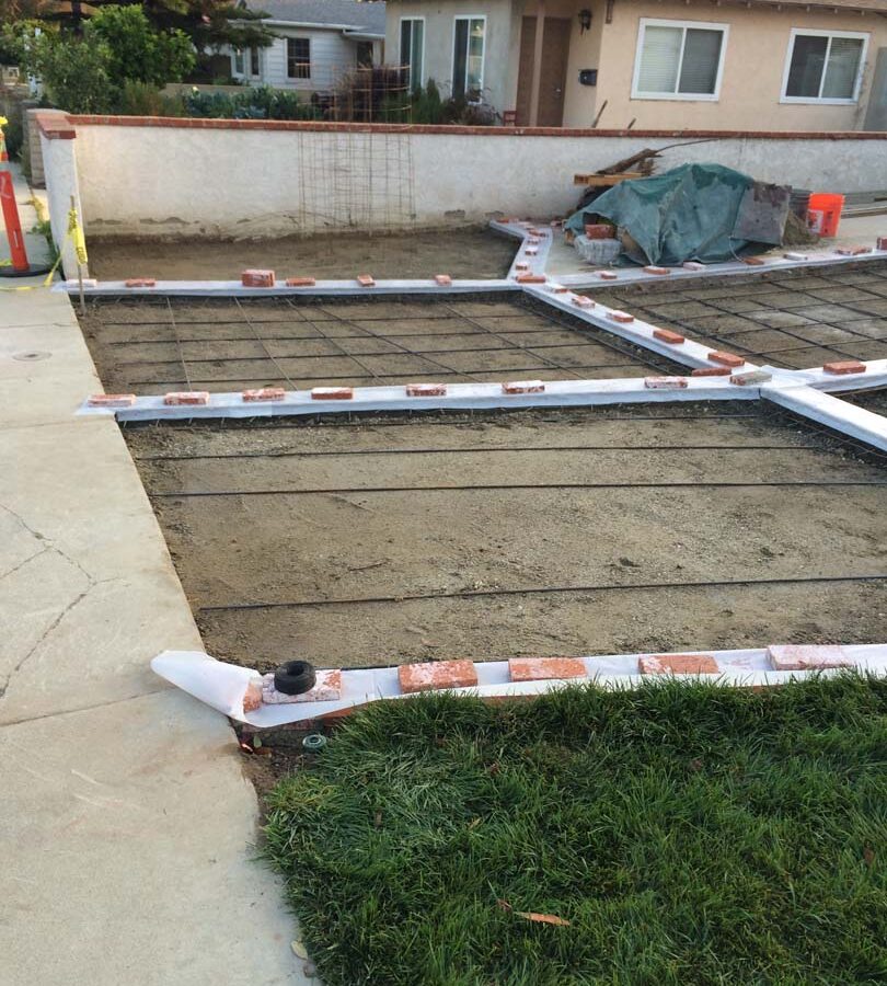 Installing steel reinforcement of a new gray concrete driveway with brick ribbons. Pacificland Constructors