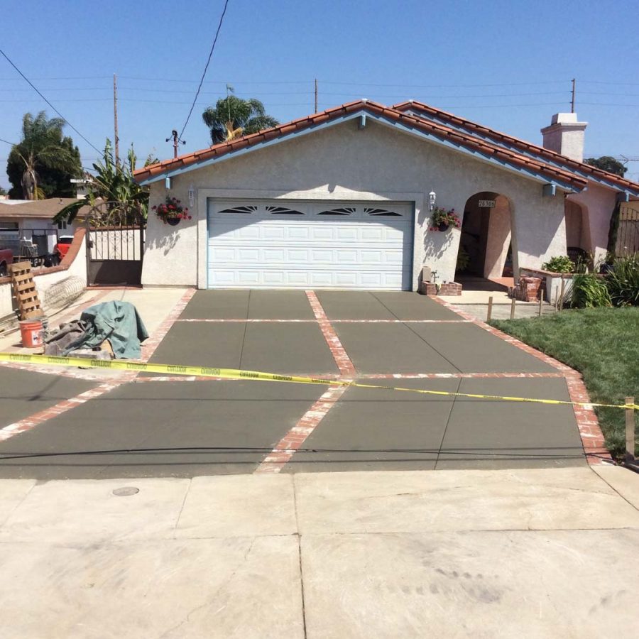 New broom swept gray concrete driveway with brick ribbons. Pacificland Constructors