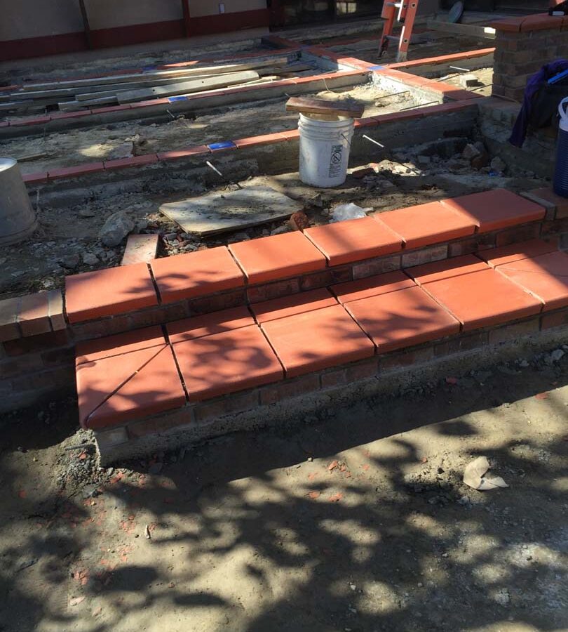 Construction of bull-nosed steps for a new broom swept gray concrete patio with brick ribbons. Pacificland Constructors