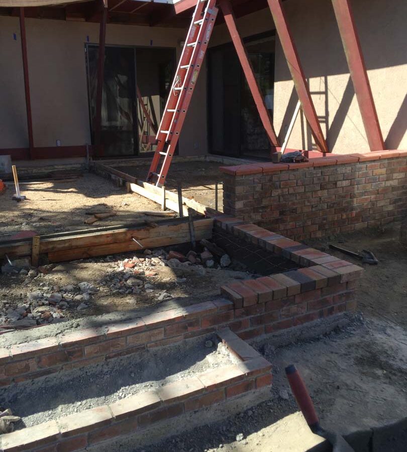 Construction of a new raised gray concrete patio with brick ribbons and brick steps. Pacificland Constructors