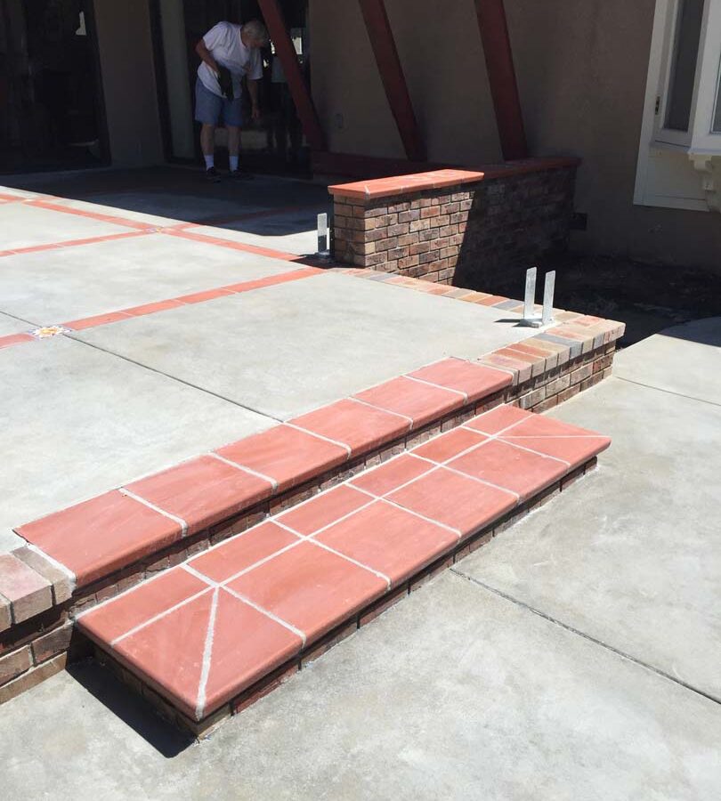 New broom swept gray concrete patio with brick ribbons and bull-nosed brick steps. Pacificland Constructors