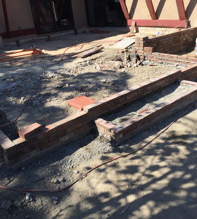 Construction of a new raised gray concrete patio with brick ribbons and brick steps. Pacificland Constructors