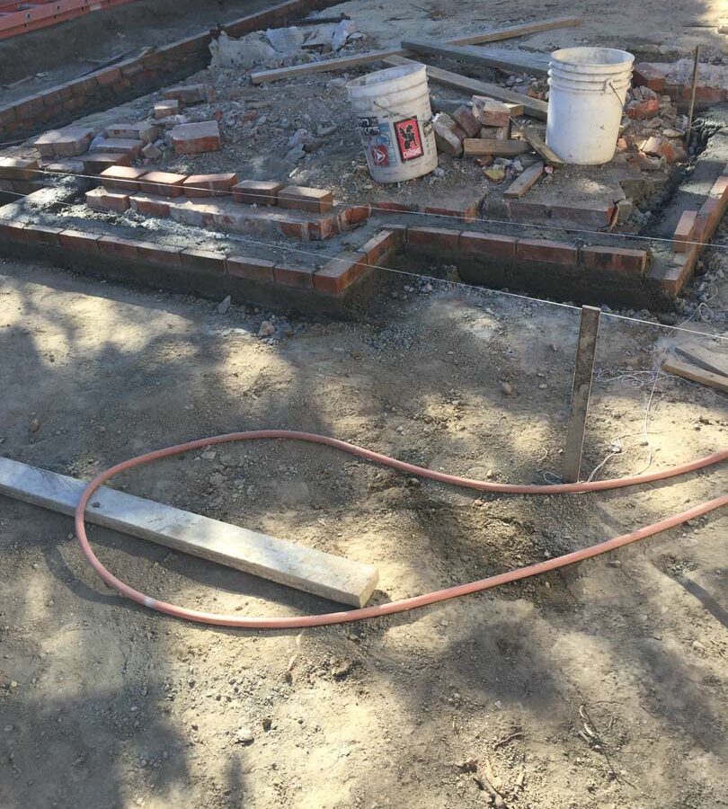 Construction of a new raised gray concrete patio with brick ribbons and brick steps. Pacificland Constructors