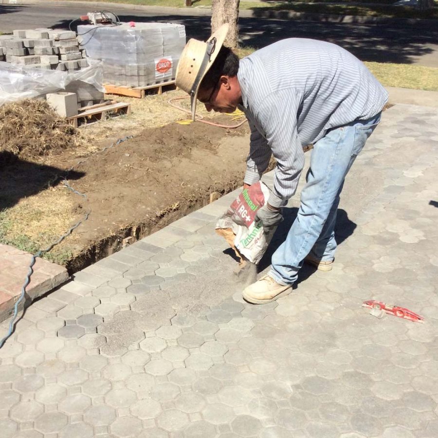 Martin, founder of Pacificland, applying silica sand between the joints of new concrete pavers for a home’s front yard. Pavers are a great option to raise the value of your home. Pacificland Constructors