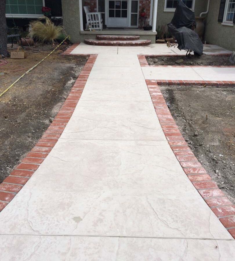 New stamped concrete front patio with brick ribbon with manufactured white stained brick ribbons and steps that creates a vintage look. Pacificland Constructors