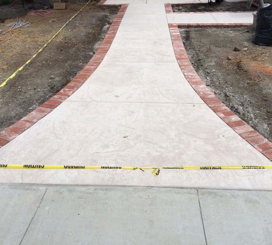 New stamped concrete walkway with brick ribbon with manufactured white stained brick ribbons that creates a vintage look. Pacificland Constructors