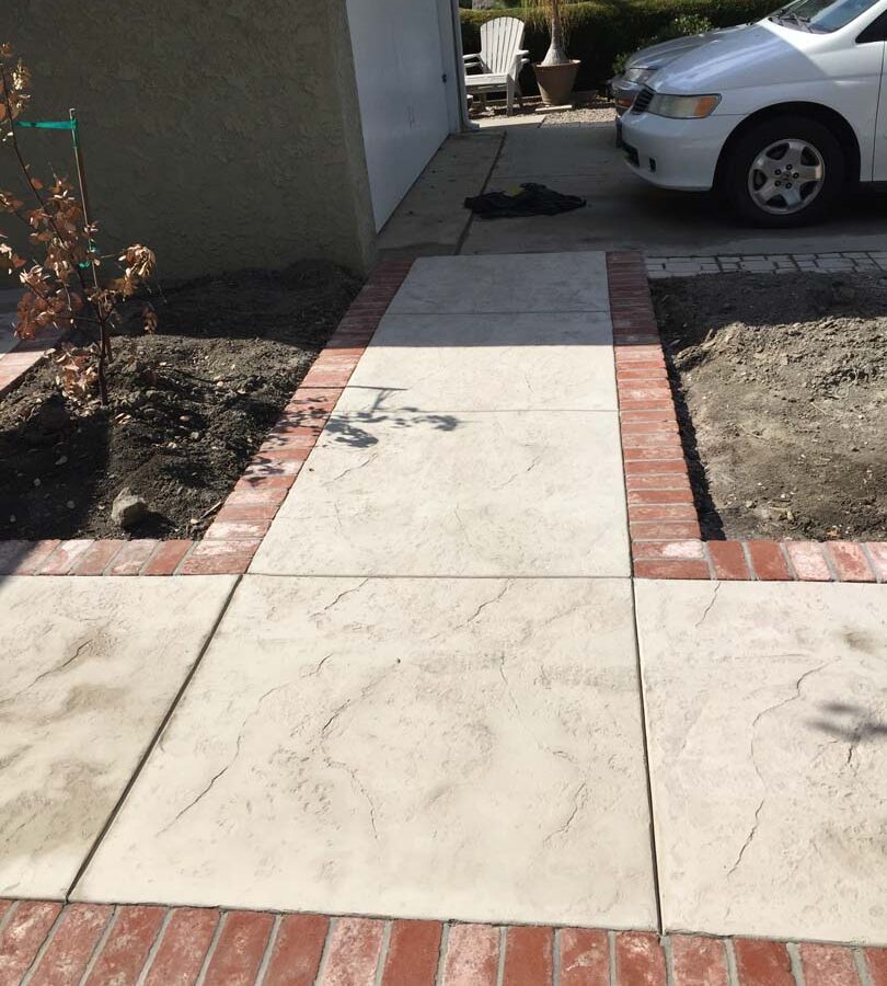 New stamped concrete walkway with brick ribbon with manufactured white stained brick ribbons that creates a vintage look. Pacificland Constructors