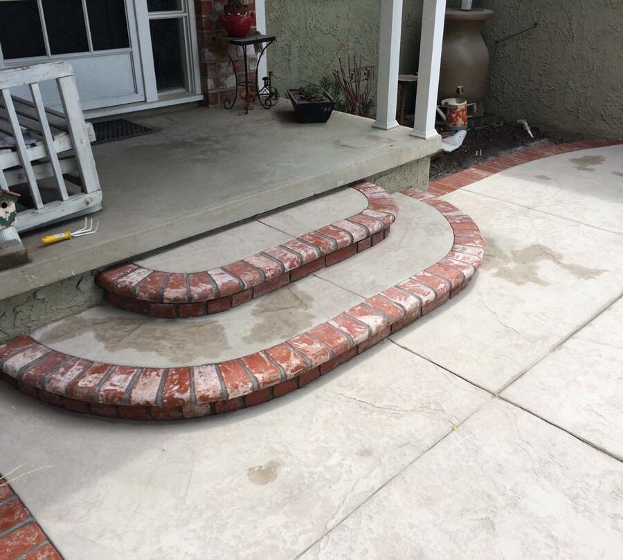 New stamped concrete front patio with brick ribbon with manufactured white stained brick ribbons and steps that creates a vintage look. Pacificland Constructors