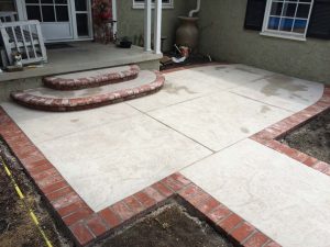 New stamped concrete front patio with brick ribbon with manufactured white stained brick ribbons and steps that creates a vintage look. Pacificland Constructors