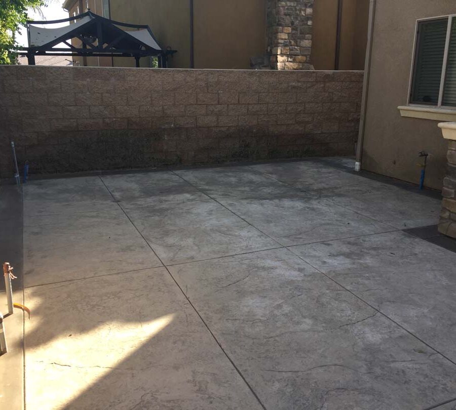 Gray stamped concrete along the side yard of the home with a new CMU tan split face block wall. Pacificland Constructors