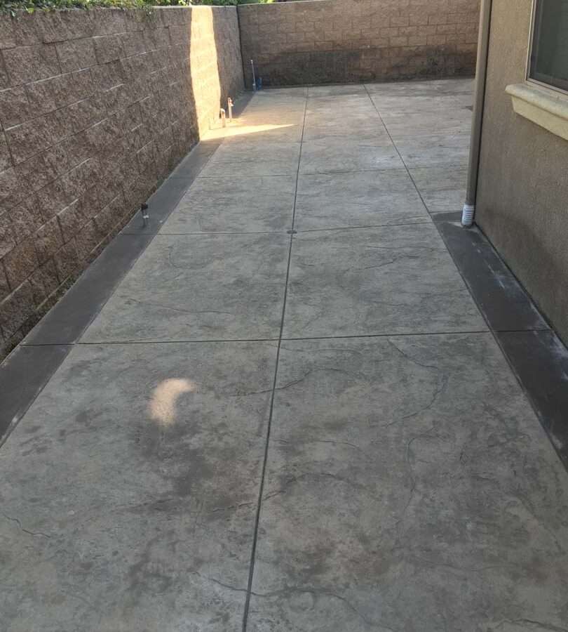 Gray stamped concrete with darker concrete ribbon and new CMU tan split face block wall. Pacificland Constructors