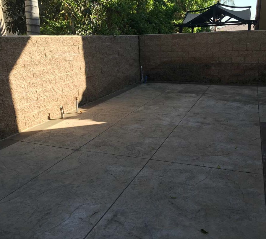 Gray stamped concrete with soffcut joints, a darker colored concrete ribbon, and a stone veneer for the backyard. Pacificland Constructors