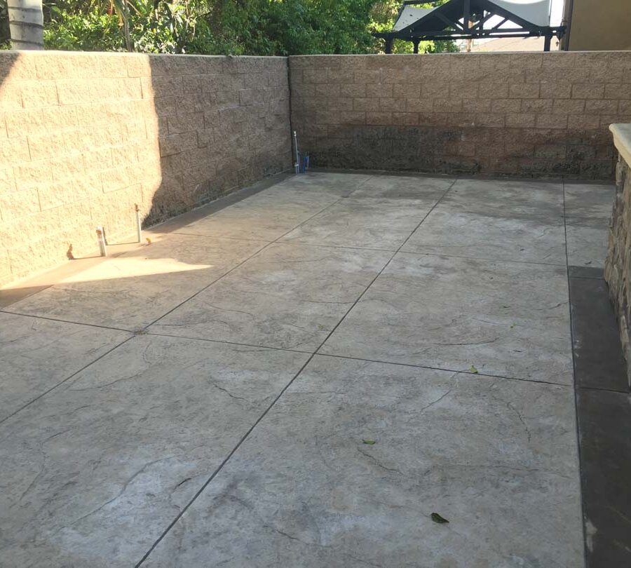 Gray stamped concrete with soffcut joints, a darker colored concrete ribbon, and a stone veneer for the backyard. Pacificland Constructors