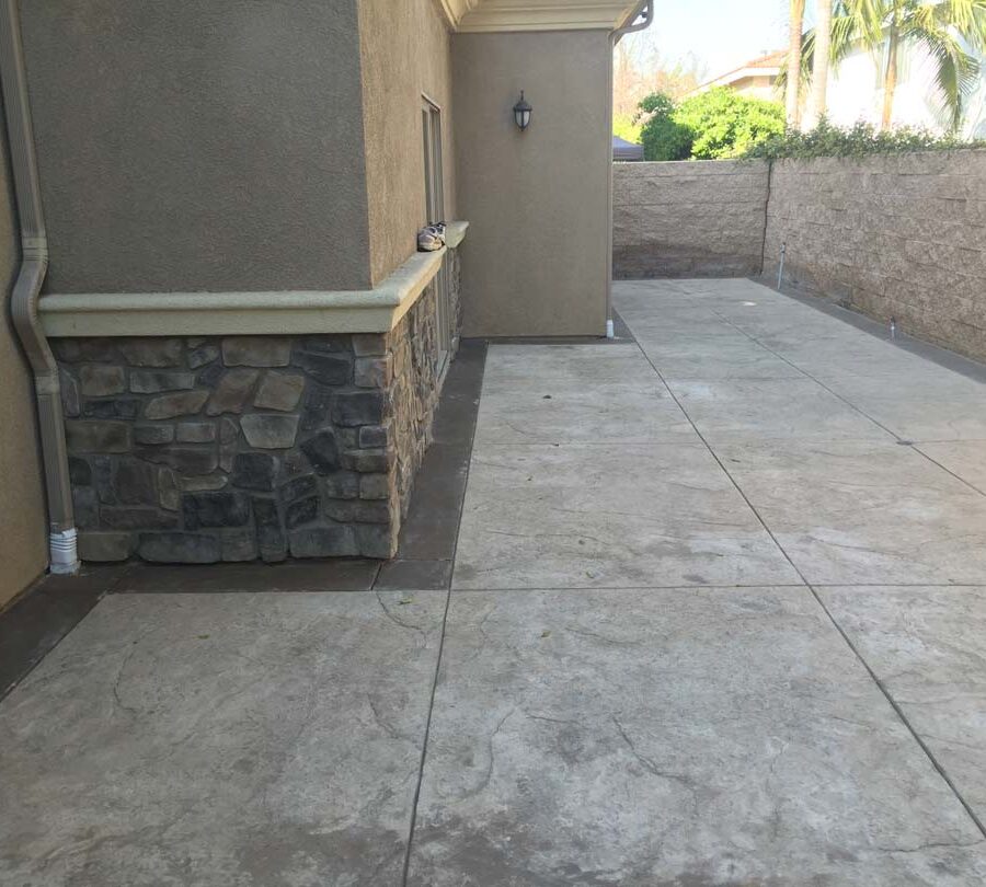 Gray stamped concrete with soffcut joints, a darker colored concrete ribbon, and a stone veneer for the backyard. Pacificland Constructors