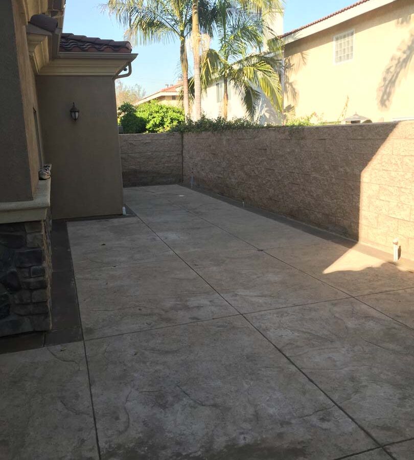 Gray stamped concrete with soffcut joints, a darker colored concrete ribbon, and a stone veneer for the backyard. Pacificland Constructors