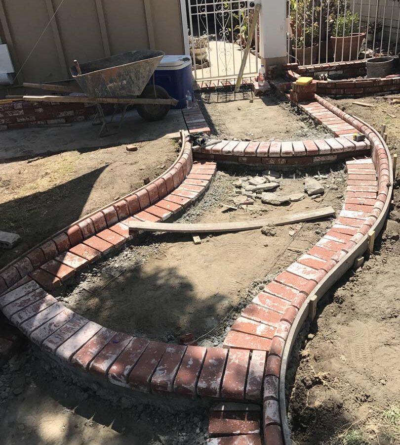 Construction of a new beautiful curved front yard concrete walkway with brick ribbon bull-nosed steps. Pacificland Constructors