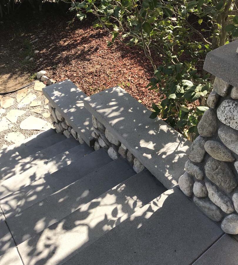 Cobble stone covered short wall topped off with a concrete poured wall cap. New concrete steps have a broom finish texture. Pacificland Constructors