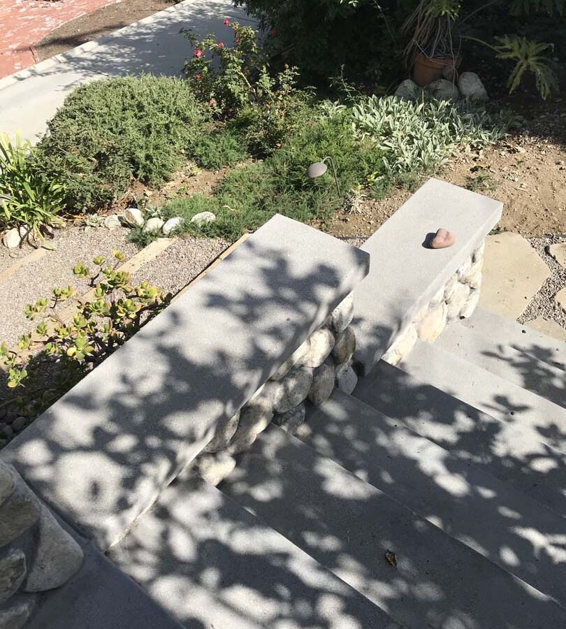 Cobble stone covered short wall topped off with a concrete poured wall cap. New concrete steps have a broom finish texture. Pacificland Constructors