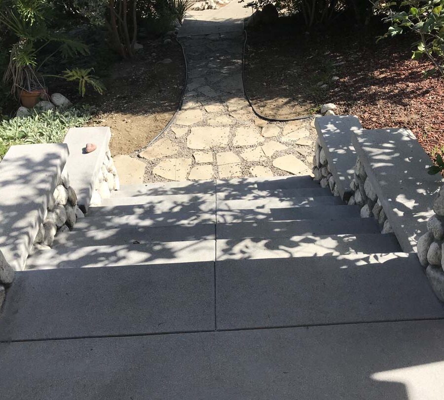 Cobble stone covered short wall topped off with a concrete poured wall cap. New concrete steps have a broom finish texture and a flagstone walkway. Pacificland Constructors