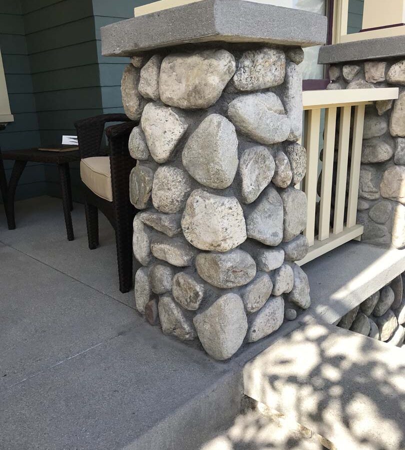 Cobble stone covered short wall topped off with a concrete poured wall cap. New concrete steps have a broom finish texture. Pacificland Constructors