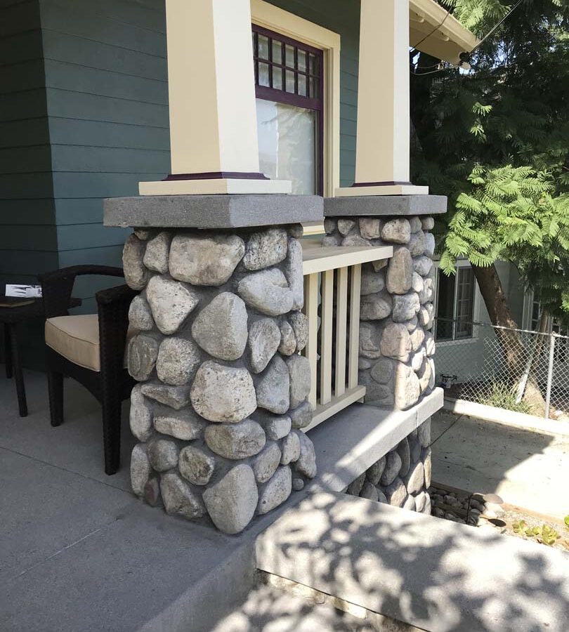 Cobble stone covered short wall topped off with a concrete poured wall cap. New concrete steps have a broom finish texture. Pacificland Constructors