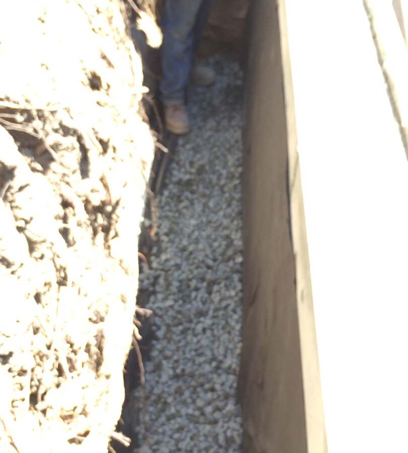 Installing a drainage system for this new retaining wall. A perforated PVC pipe is buried under the porous aggregate that will collect the water that accumulates behind the wall and drain it out. This allows the wall to maintain its structural integrity throughout the years. Pacificland Constructors