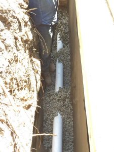 Installing a drainage system for this new retaining wall. A perforated PVC pipe is buried under the porous aggregate that will collect the water that accumulates behind the wall and drain it out. This allows the wall to maintain its structural integrity throughout the years. Pacificland Constructors