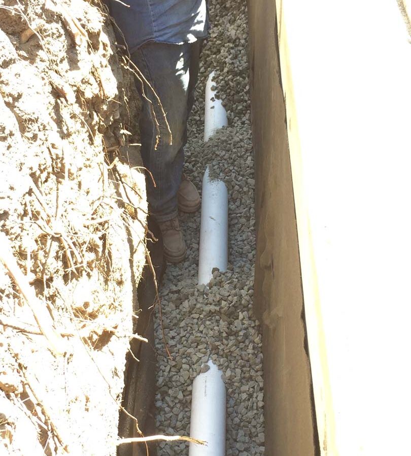 Installing a drainage system for this new retaining wall. A perforated PVC pipe is buried under the porous aggregate that will collect the water that accumulates behind the wall and drain it out. This allows the wall to maintain its structural integrity throughout the years. Pacificland Constructors