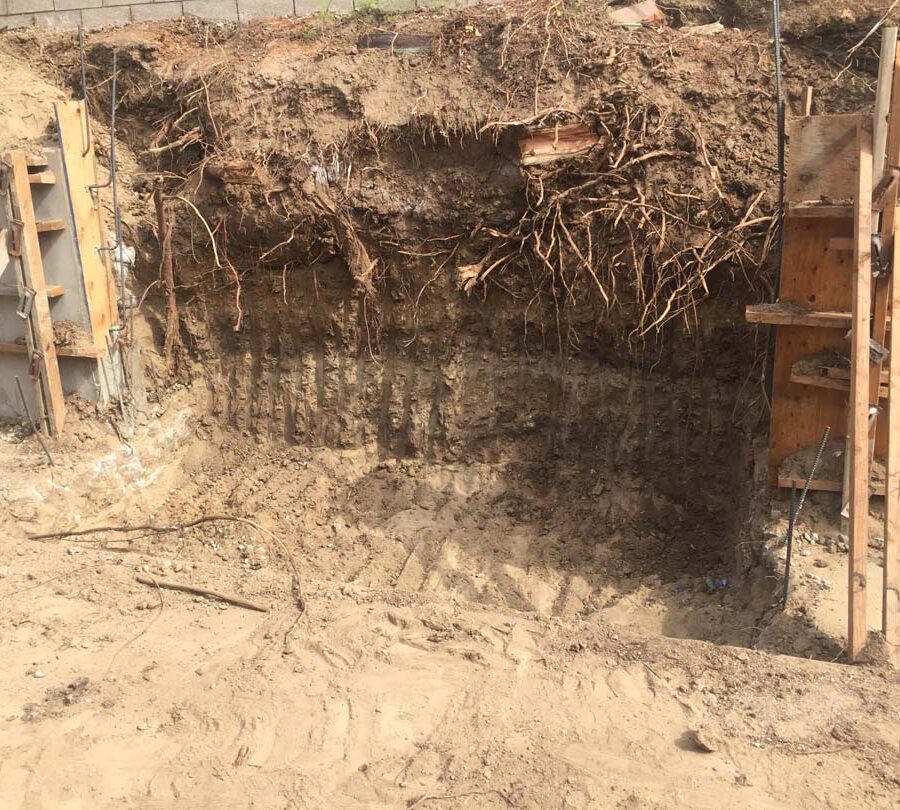 Excavating for a new section of concrete retaining wall. This must be done in sections to avoid having the uneven soil collapse. Pacificland Constructors