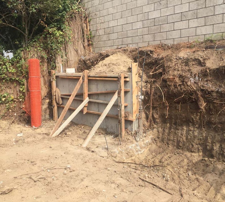 Excavating for a new section of concrete retaining wall. This must be done in sections to avoid having the uneven soil collapse. Pacificland Constructors