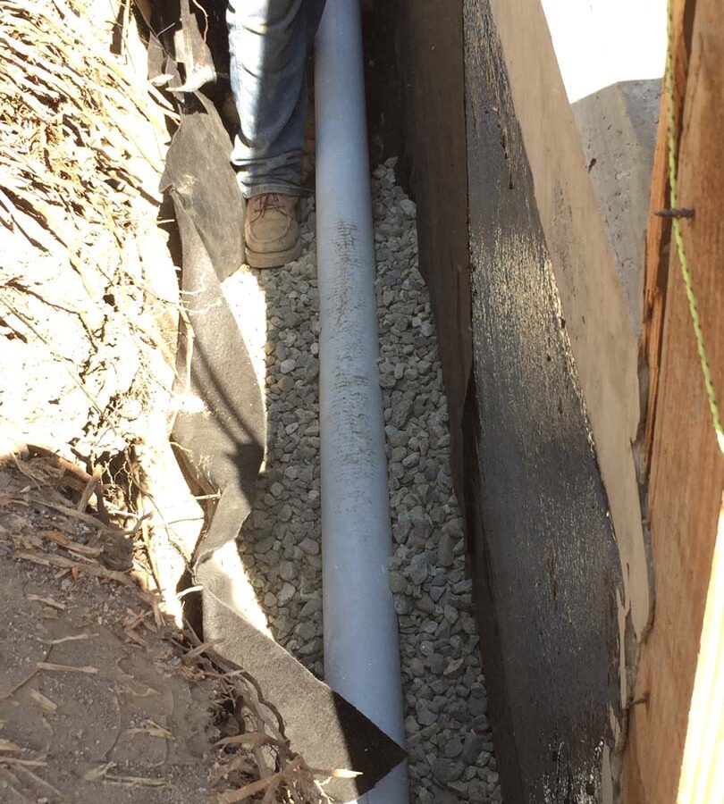 Installing a drainage system for this new retaining wall. This perforated PVC pipe is buried under a porous aggregate that will serve as a filter for water before it is collected by the PVC pipe and drained out from behind the wall. This allows the wall to maintain its structural integrity throughout the years. Pacificland Constructors