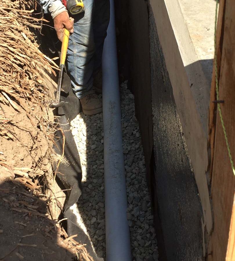 Installing a drainage system for this new retaining wall. This perforated PVC pipe is buried under a porous aggregate that will serve as a filter for water before it is collected by the PVC pipe and drained out from behind the wall. This allows the wall to maintain its structural integrity throughout the years. Pacificland Constructors