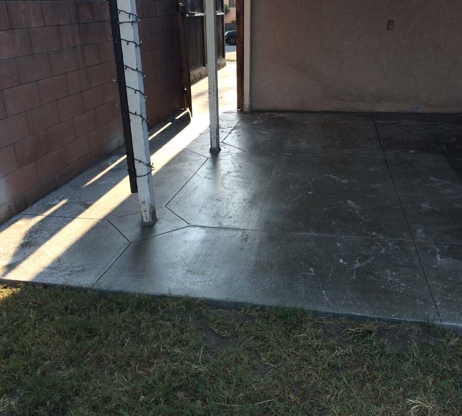 New beautiful broom swept concrete backyard patio with a handmade joint pattern and sealer polymer being applied to it. This polymer will become transparent when dry and protect the concrete from stains while creating a somewhat reflective surface as if it were just watered. Pacificland Constructors