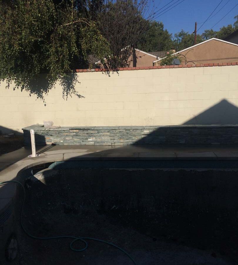 New gray concrete deck with a stone veneered planter with custom colored wall cap. Pacificland Constructors